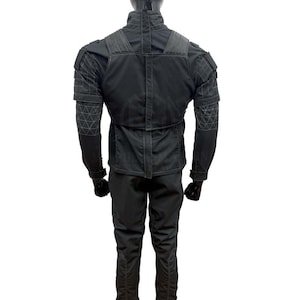 May include: A black tactical jacket and pants set. The jacket features a high collar, reinforced shoulders, and geometric stitching on the sleeves. The pants have a streamlined design. The outfit is made of a matte, durable material.