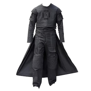 Puede incluir: Un conjunto de disfraz negro con un top corto con un dise&ntilde;o geom&eacute;trico, una camisa de manga larga y pantalones con rodilleras acolchadas y bolsillos. El conjunto incluye un abrigo largo y fluido. Costuras blancas acent&uacute;an la tela oscura.