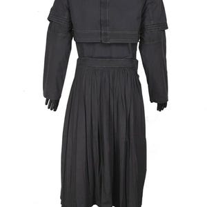 May include: A black ensemble featuring a long-sleeved jacket with shoulder detailing, a pleated skirt, and matching pants. The jacket has a unique layered design, and the outfit is made of a solid, dark fabric.