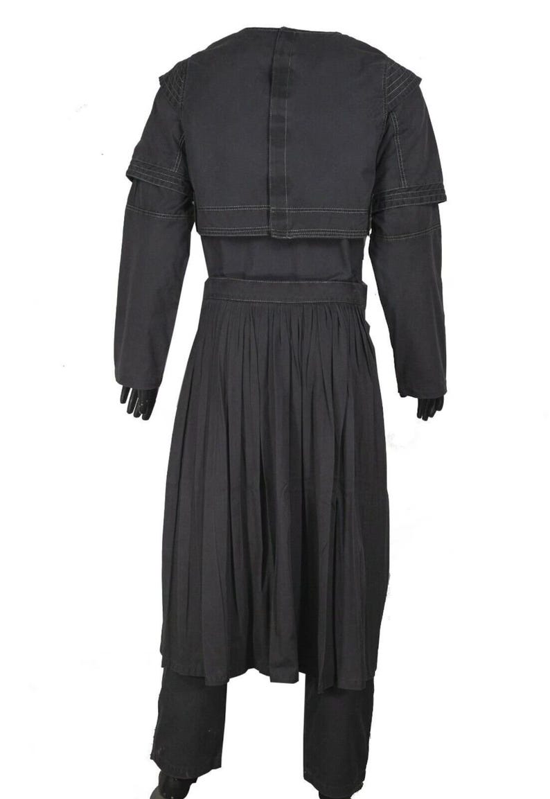 May include: A black ensemble featuring a long-sleeved jacket with shoulder detailing, a pleated skirt, and matching pants. The jacket has a unique layered design, and the outfit is made of a solid, dark fabric.