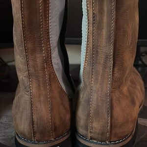 K&ouml;nnte beinhalten: Paar braune Lederstiefel mit Used-Look. Die Stiefel haben einen seitlichen Rei&szlig;verschluss, graue Akzente und eine schwarze Sohle. Jeder Stiefel hat ein Gr&ouml;&szlig;enschild mit der Nummer 45. Die Stiefel sind f&uuml;r den Au&szlig;enbereich konzipiert.
