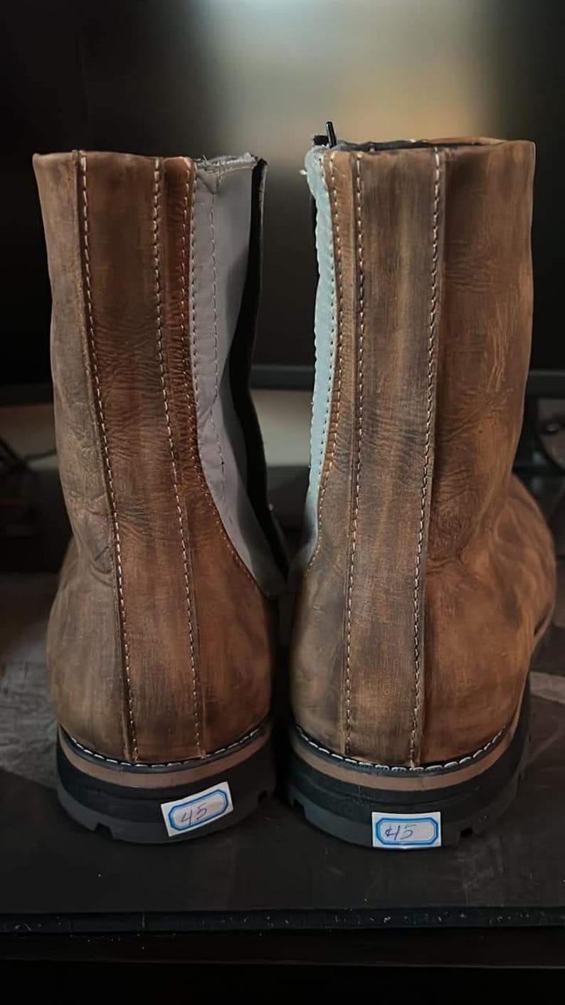 K&ouml;nnte beinhalten: Paar braune Lederstiefel mit Used-Look. Die Stiefel haben einen seitlichen Rei&szlig;verschluss, graue Akzente und eine schwarze Sohle. Jeder Stiefel hat ein Gr&ouml;&szlig;enschild mit der Nummer 45. Die Stiefel sind f&uuml;r den Au&szlig;enbereich konzipiert.