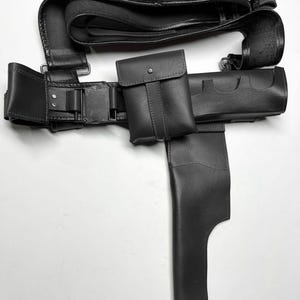 Puede incluir: Un cintur&oacute;n utilitario de cuero negro con m&uacute;ltiples bolsas, una funda y portacartuchos. El cintur&oacute;n presenta un cierre de hebilla y est&aacute; dise&ntilde;ado para transportar varios objetos. El dise&ntilde;o general es elegante y funcional.