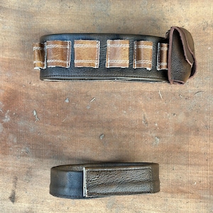 May include: Two-piece leather belt set. The main belt is dark brown with lighter brown rectangular accents and a small pouch. The second piece is a matching dark brown belt.