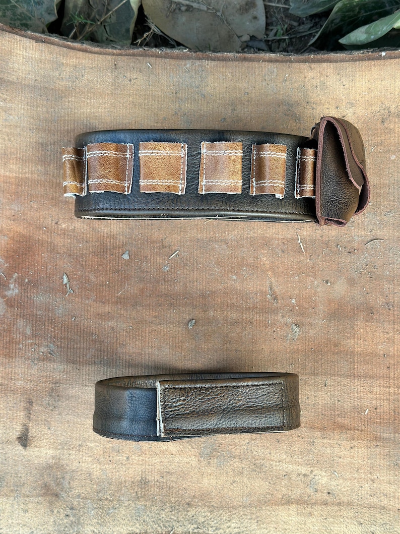 May include: Two-piece leather belt set. The main belt is dark brown with lighter brown rectangular accents and a small pouch. The second piece is a matching dark brown belt.