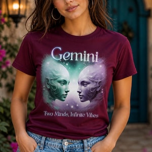 Op de afbeelding: Bordeauxrode t-shirt met een Gemini-ontwerp. De afbeelding toont twee etherische gezichten tegenover elkaar, met het woord "Gemini" erboven en de tekst "Two Minds, Infinite Vibes" eronder. Het ontwerp heeft een hemels thema.