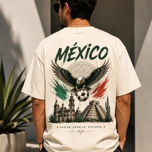 May include: A cream-colored t-shirt featuring a graphic on the back with the word M&Eacute;XICO, an eagle holding a soccer ball, a cathedral, a pyramid, and green and red brushstrokes. The text reads PASI&Oacute;N. ORGULLO. HISTORIA. and 2026 at the bottom.