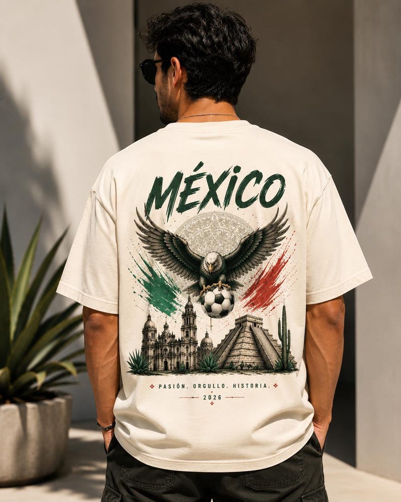 May include: A cream-colored t-shirt featuring a graphic on the back with the word M&Eacute;XICO, an eagle holding a soccer ball, a cathedral, a pyramid, and green and red brushstrokes. The text reads PASI&Oacute;N. ORGULLO. HISTORIA. and 2026 at the bottom.