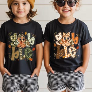 May include: Two black t-shirts featuring a graphic of a turkey and the text "gobble" in patterned letters. One shirt is paired with a mustard yellow beanie, and the other with black sunglasses. Both shirts are worn with black and white gingham shorts.