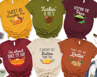May include: Six short-sleeve t-shirts in mustard yellow, olive green, maroon, dark red, cream, and burnt orange. Each shirt features a unique graphic print with text including Sweet as Pumpkin Pie, Turkin' 9 to 5, Keeping the Peas, Go ahead BAKE MY DAY, IT DOESN'T GET Butter THAN THIS, and THEY SEE ME Rollin'.
