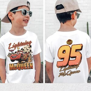 Pu&ograve; includere: T-shirt bianca con Lightning McQueen del film Cars. La parte anteriore presenta il testo "Lightning McQueen" e un design di auto da corsa. Il retro mostra il numero "95" e il testo "Lightning McQueen".