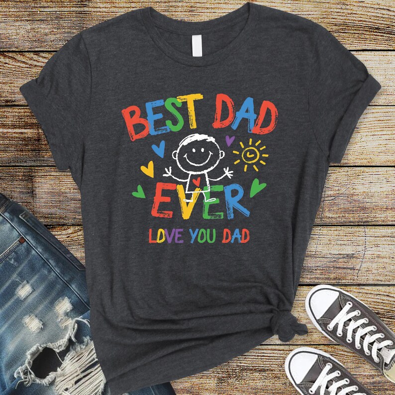 May include: Dark gray t-shirt with the words "BEST DAD EVER" in colorful block letters. A stick figure with a smiling face is in the center, with hearts and a sun graphic. The text "LOVE YOU DAD" is below the graphic.