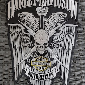 Puede incluir: Parche de Harley-Davidson en blanco y negro con una calavera con rayos cruzados, alas y las palabras "HARLEY-DAVIDSON MOTORCYCLES". El parche tiene forma de escudo con una corona en la parte superior.