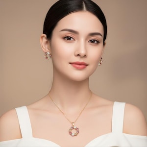 Puede incluir: Un conjunto de collar y pendientes dorados. El colgante y los pendientes presentan un diseño circular con piedras preciosas de colores. La joyería se destaca sobre un fondo neutro.
