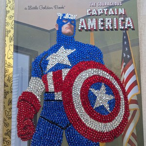 May include: A Little Golden Book titled "The Courageous Captain America." The cover features a bedazzled Captain America with his shield and the American flag in the background. The book is a Marvel product.