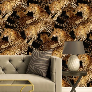 Könnte beinhalten: Ein beiges Sofa mit gesteppter Rückenlehne und einem kissen mit Zebrastreifen steht vor einer Wand mit Leopardenmuster. Neben dem Sofa steht ein kleiner Beistelltisch mit einer Lampe. Die Lampe hat einen grauen Schirm und einen strukturierten weißen Sockel.