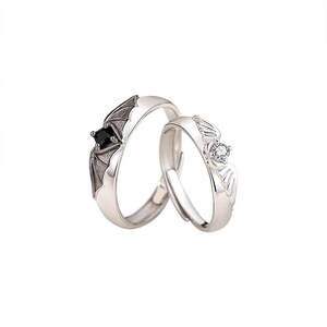 May include: Two silver rings, one with a bat wing design and a black square stone, the other with a wing design and a clear round stone. The rings are set against a white background.
