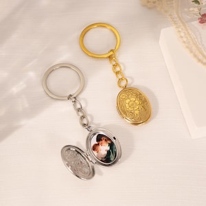 May include: Two oval locket keychains, one gold-toned and one silver-toned. The gold locket features an embossed floral pattern on the front. The silver locket is open, revealing a small photograph of two people inside, attached to a circular ring.