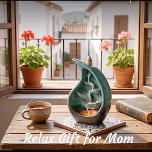 May include: A teal ceramic incense burner with a waterfall design, a lit candle, and a cup of tea on a wooden table. The text "Relax Gift for Mom" is visible. Potted flowers are in the background.