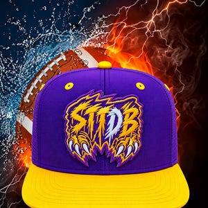 May include: A purple baseball cap with a yellow brim and yellow eyelets. The front features an embroidered patch with the text STIDB in a jagged, claw-like font, colored in yellow and white with purple outlines, set against a background of water and fire.