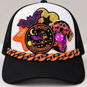 May include: A black and white trucker hat featuring a central circular patch with a dachshund on a broomstick and the text Happy Halloweenie. The hat is decorated with a sequined orange star, a purple bat, and a dog wearing star-shaped glasses.