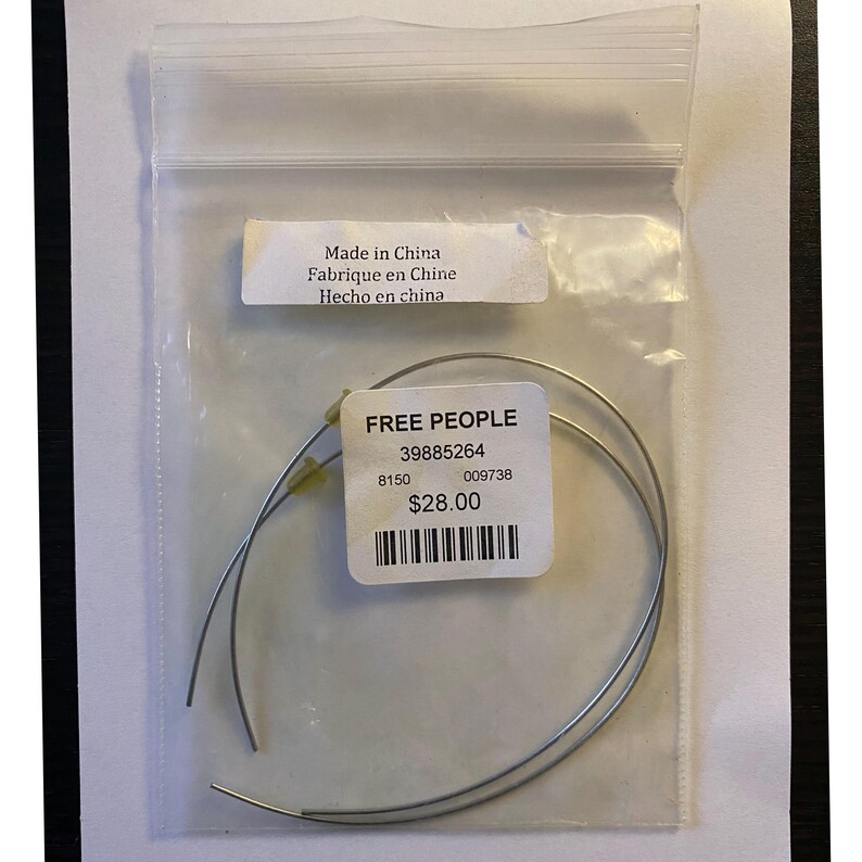 May include: A clear plastic bag containing two silver-colored, curved metal pieces. A white label with the text "FREE PEOPLE" and other details is attached. The bag also has a label that says "Made in China".