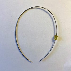 May include: A silver-colored metal headband with a small, yellow plastic piece attached. The headband is curved and open at the bottom. The background is a plain, light-colored surface.