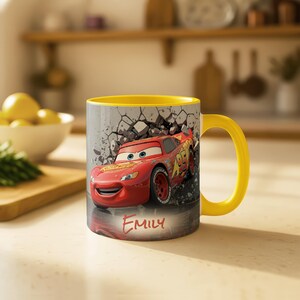 May include: A yellow-handled mug featuring Lightning McQueen from the Cars movie, bursting through a cracked wall design. The mug has a yellow interior and the name "Emily" is written on the front.