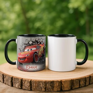 May include: Two ceramic mugs with black handles and rims. One mug features a red race car graphic with the name "Emily" below. The other mug is plain white. Both mugs are on a wooden surface.
