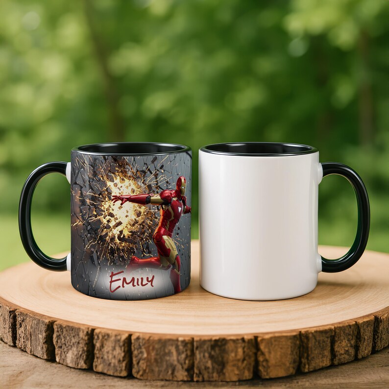 May include: Two ceramic coffee mugs. One mug features a red and gold Iron Man design with the name "Emily" in red script. The other mug is plain white with a black handle and rim. Both mugs are on a wooden surface.