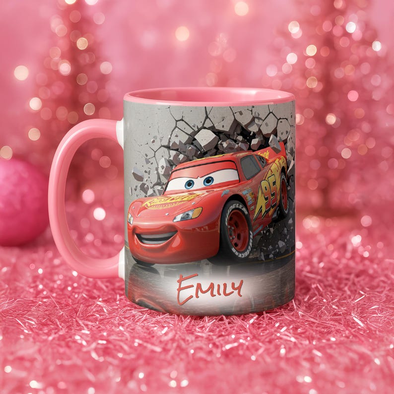 May include: A ceramic mug with a pink handle and interior. The mug features a graphic of the character Lightning McQueen from the movie Cars, bursting through a wall. The name "Emily" is written on the mug.