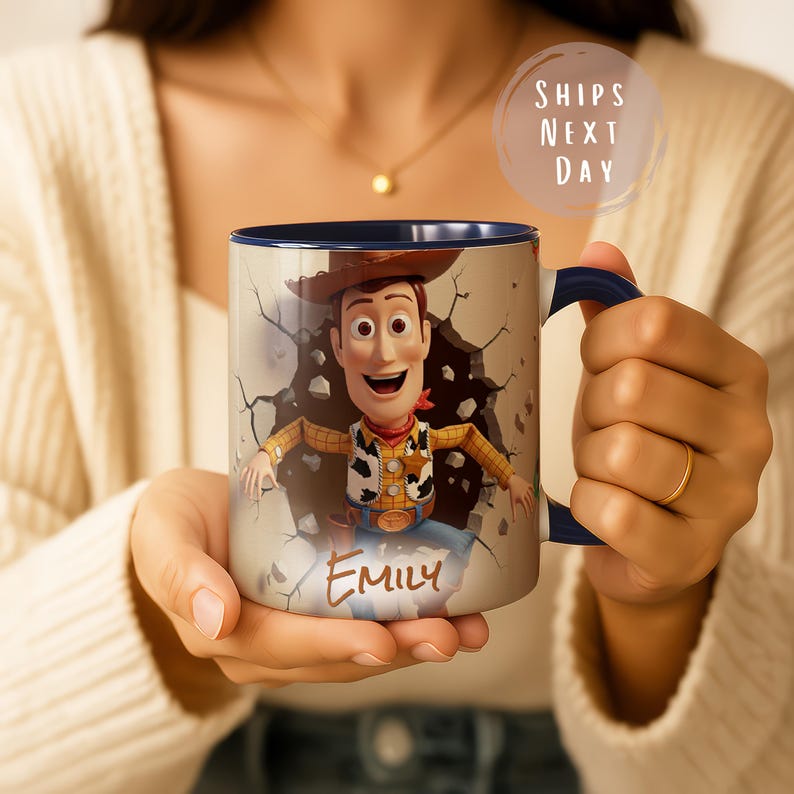 May include: A ceramic mug with a cartoon cowboy design, breaking through a wall. The mug has a navy blue handle and interior. The name "Emily" is printed on the front. The mug is a standard size for hot beverages.