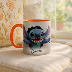 Puede incluir: Taza de cer&aacute;mica blanca con interior y asa naranja. La taza presenta una imagen 3D del personaje de Disney Stitch rompiendo un agujero, con el nombre "Emily" escrito debajo en azul.