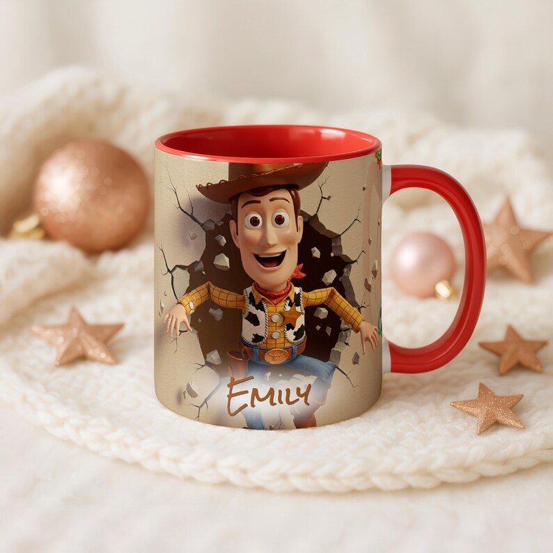 May include: A ceramic mug with a red interior and handle, featuring a cartoon image of Woody from Toy Story breaking through a wall. The name "Emily" is printed on the mug.