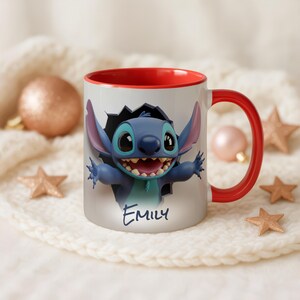 Puede incluir: Una taza de cer&aacute;mica blanca con interior y asa rojos. La taza presenta un personaje de dibujos animados azul saliendo de un agujero, con el nombre "Emily" escrito debajo. La taza est&aacute; rodeada de adornos decorativos.