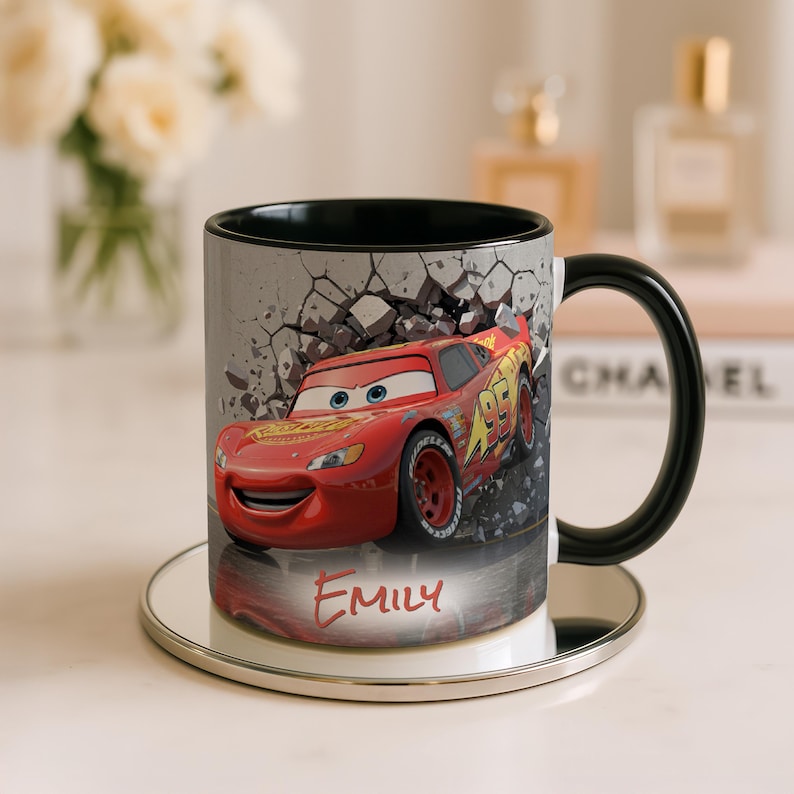May include: A ceramic mug featuring Lightning McQueen from the Cars movie. The red and yellow race car is set against a gray, cracked wall design. The mug has a black handle and interior, with the name "Emily" in red.