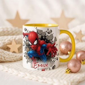 K&ouml;nnte beinhalten: Wei&szlig;e Keramiktasse mit gelbem Innenraum und Henkel. Die Tasse zeigt eine farbenfrohe Illustration von Spider-Man, der durch eine Wand bricht, mit dem Namen "EMILY" in roter Schrift. Dekorative Ornamente und Sterne sind im Hintergrund.