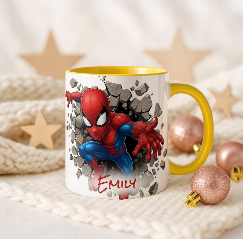 K&ouml;nnte beinhalten: Wei&szlig;e Keramiktasse mit gelbem Innenraum und Henkel. Die Tasse zeigt eine farbenfrohe Illustration von Spider-Man, der durch eine Wand bricht, mit dem Namen "EMILY" in roter Schrift. Dekorative Ornamente und Sterne sind im Hintergrund.