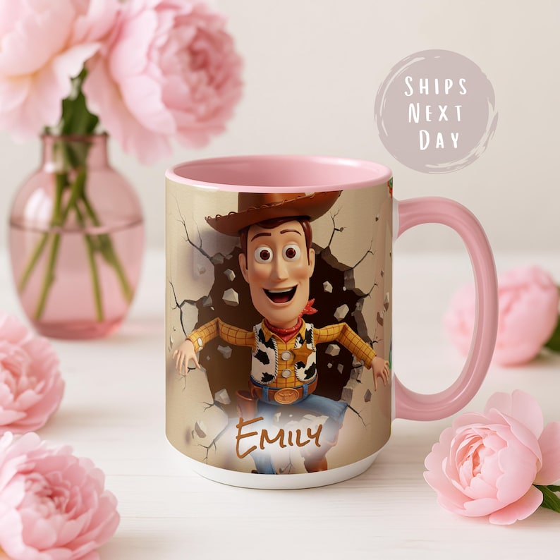 May include: A ceramic mug with a cartoon image of Woody breaking through a wall. The mug has a pink handle and interior. The name "Emily" is written on the front. The background includes pink flowers in a vase.