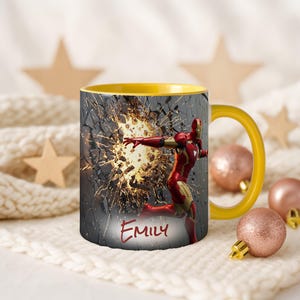 May include: A yellow-handled coffee mug featuring Iron Man breaking through a wall. The mug has a yellow interior and the name "Emily" is written on the front. The design includes a red and gold Iron Man figure.
