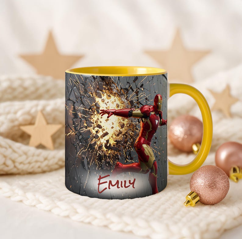 May include: A yellow-handled coffee mug featuring Iron Man breaking through a wall. The mug has a yellow interior and the name "Emily" is written on the front. The design includes a red and gold Iron Man figure.