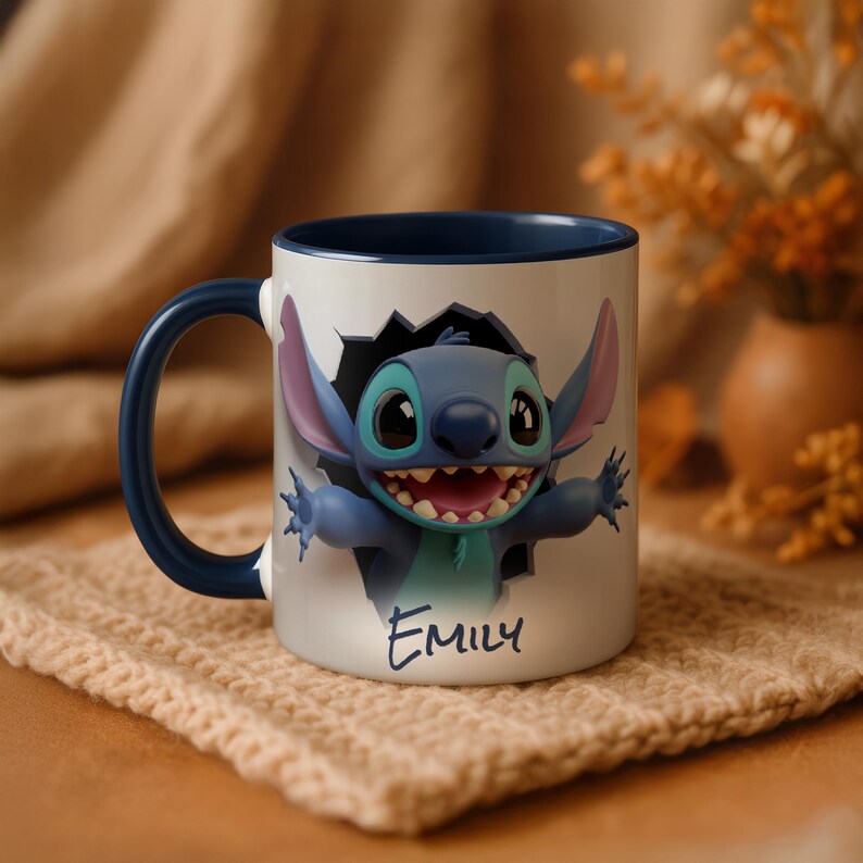Puede incluir: Una taza de cer&aacute;mica blanca con interior y asa azules. La taza presenta una imagen 3D del personaje Stitch rompiendo una pared. El nombre "Emily" est&aacute; escrito en gui&oacute;n azul en la taza.