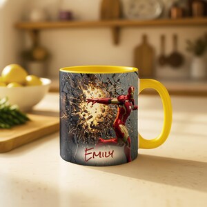 May include: Yellow-handled coffee mug featuring Iron Man breaking through a wall. The mug has a yellow interior and the name "Emily" is written on the front.