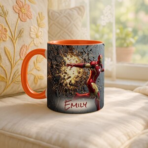 May include: Orange-handled mug featuring Iron Man in a dynamic pose against a cracked wall background. The mug's interior is orange, and the name "Emily" is written in red script. A superhero-themed coffee mug.