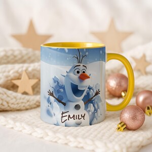 May include: A white ceramic mug with a yellow handle and interior. The mug features a cartoon image of Olaf from Frozen, with the name "Emily" printed below. The background shows a snowy scene.