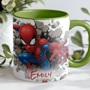 K&ouml;nnte beinhalten: Wei&szlig;e Keramik-Tasse mit einem Spiderman-Motiv, das durch eine Wand bricht. Innen und Henkel sind gr&uuml;n. Der Name "Emily" steht in roter Schrift auf der Vorderseite der Tasse.