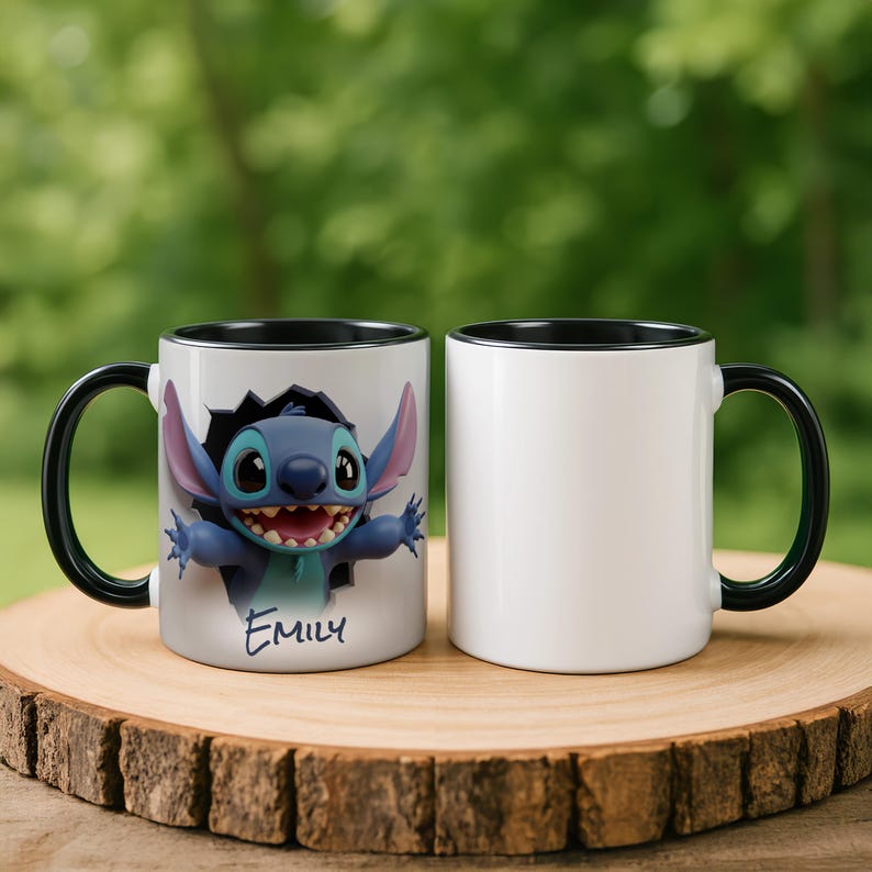 Puede incluir: Dos tazas de cer&aacute;mica blanca con asas y bordes negros. Una taza presenta una imagen 3D de un personaje de dibujos animados azul con el nombre "Emily" debajo. La otra taza es blanca lisa. Ambas tazas est&aacute;n sobre una superficie de madera.