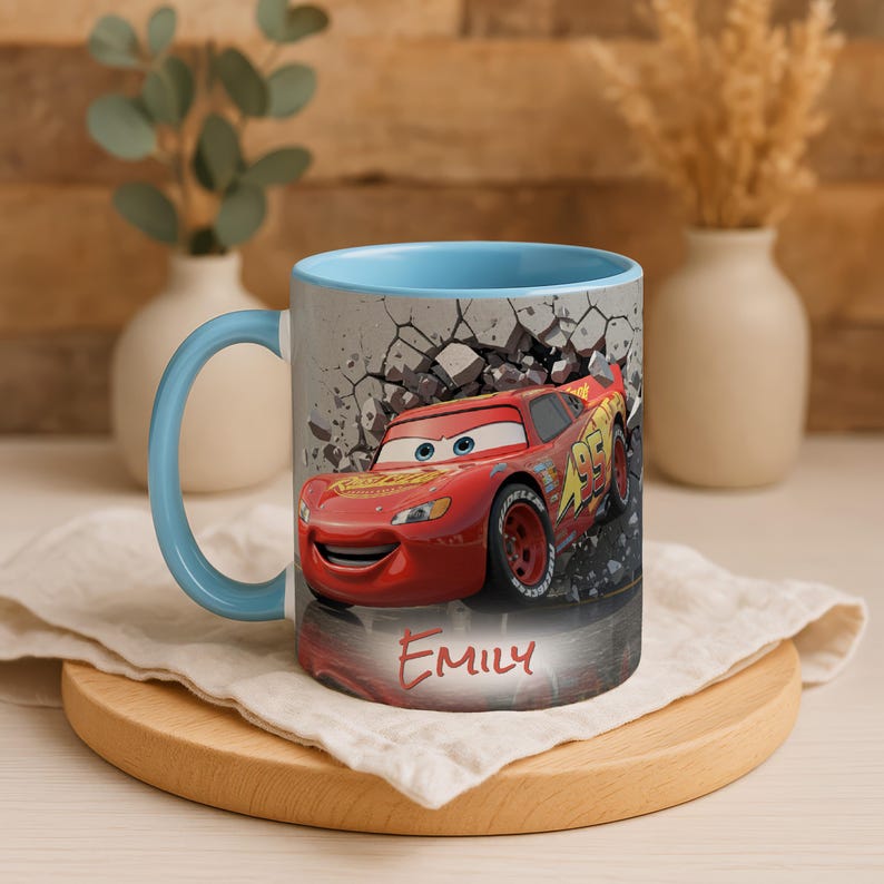 May include: A ceramic mug with a light blue interior and handle. The exterior features a red race car graphic with the name "EMILY" in red. The background shows a cracked wall.