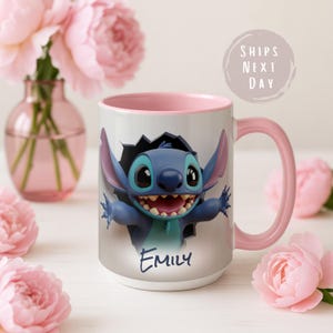 Puede incluir: Una taza de cer&aacute;mica blanca con interior y asa rosas. La taza presenta un personaje de dibujos animados azul rompiendo una pared, con el nombre "Emily" escrito debajo. El fondo incluye flores rosas y un jarr&oacute;n.