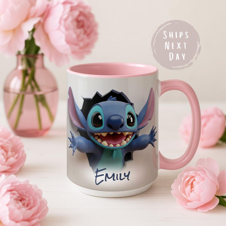 Puede incluir: Una taza de cer&aacute;mica blanca con interior y asa rosas. La taza presenta un personaje de dibujos animados azul rompiendo una pared, con el nombre "Emily" escrito debajo. El fondo incluye flores rosas y un jarr&oacute;n.